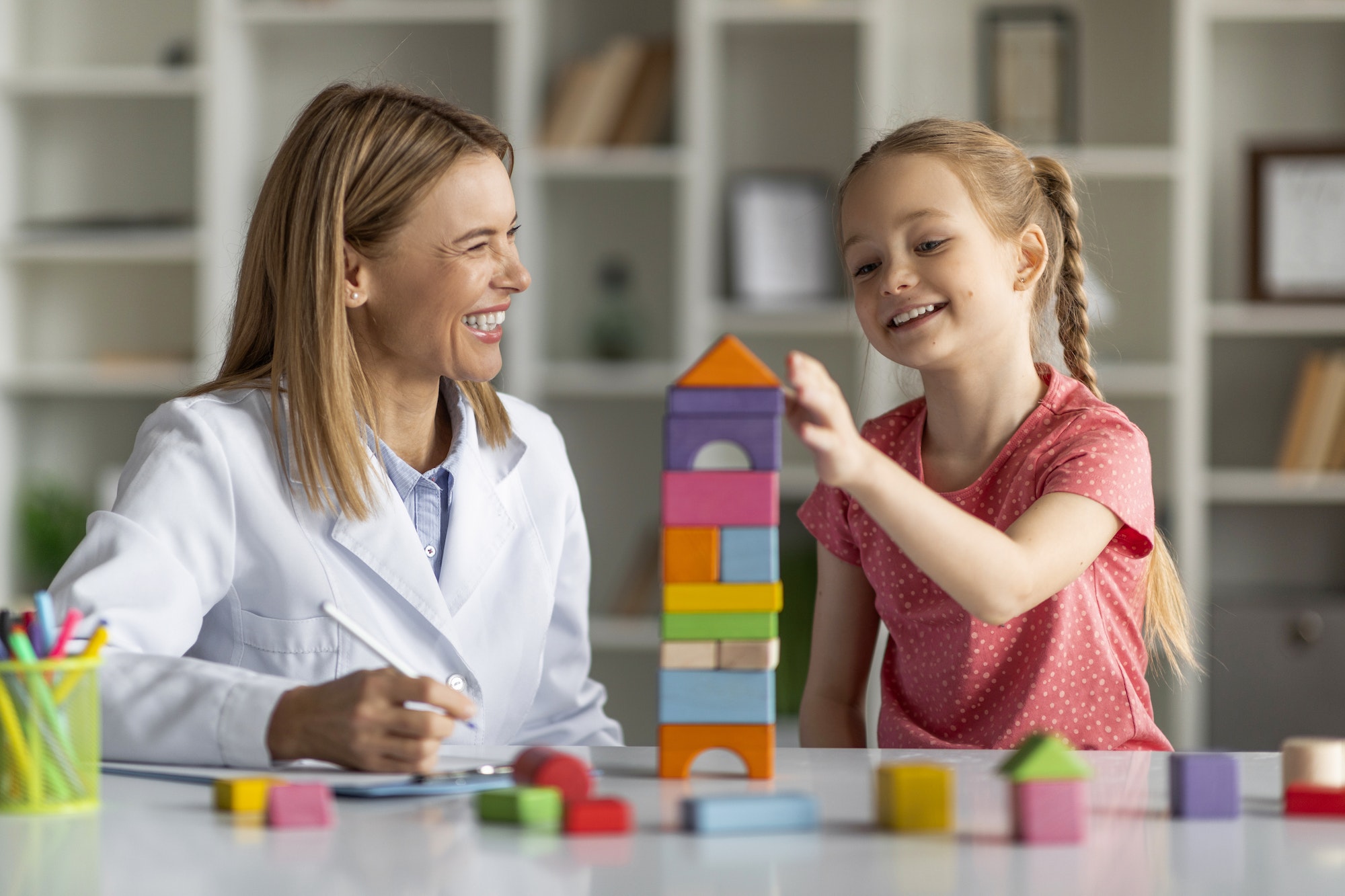 Child Development Specialist Looking At Little Girl Playing With Colorful Wooden Bricks